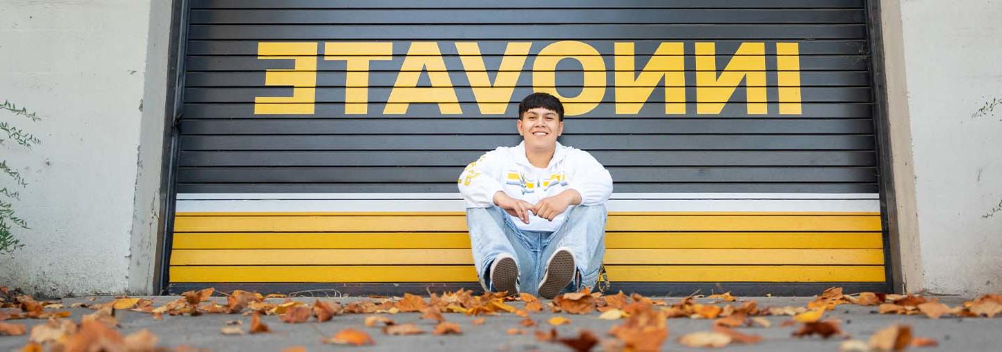 A University of Idaho student sits outside on the ground in front of a sign that says innovate.